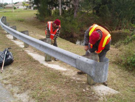 Photo of two workers repairing a metal road guardrail